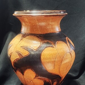 Könnte beinhalten: Eine braune Keramikvase mit schwarzer Glasur und einem floralen Design. Die Vase hat eine breite Öffnung und einen runden Körper.