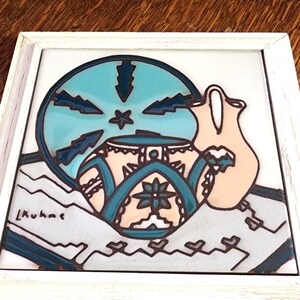 May include: A framed ceramic tile with a blue and white design of a pitcher and a bowl with a stylized floral pattern. The tile is signed "L. Kuhae".