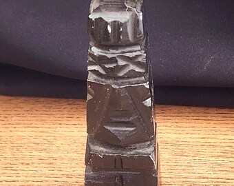 May include: A small, dark wood carved tiki statue with a human-like face and a simple design.