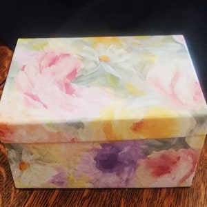May include: A rectangular box with a floral design. The box is covered in a white background with pink, yellow, and purple flowers.