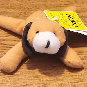 May include: A small, tan and brown beanbag plush toy dog named "Patsy". The dog has a white face with a black nose and black eyes. The tag reads "Patsy Bean Bag Friends Itsy Bitsy Collectors".