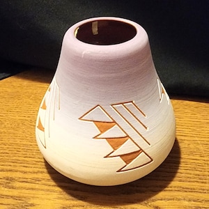 May include: A small, purple and white ceramic vase with a geometric design in orange. The vase is hand-painted and has a rounded shape.