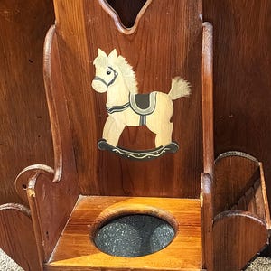 May include: Wooden potty chair with a rocking horse painted on the front. The chair has a heart-shaped cutout in the back and a small shelf on the side.