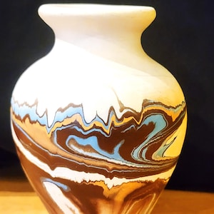 May include: A ceramic vase with a cream-coloured top and a swirling pattern of brown, blue, and tan colours. The vase has a rounded body and a narrow neck, suitable for displaying flowers or as a decorative piece.