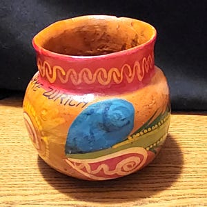 Puede incluir: Una pequeña maceta de terracota pintada a mano con un borde rojo y un diseño azul, verde y amarillo. La maceta tiene las palabras "Lake Zurich" escritas en ella.