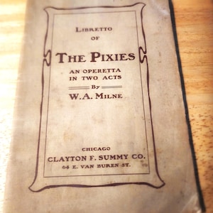 以下が含まれることがあります： W.A.ミルン作のオペレッタ「The Pixies」の古い紙製台本。表紙には濃い茶色の文字と装飾的な枠線が薄茶色の背景に描かれており、シカゴの出版社Clayton F. Summy Co.の詳細が記載されています。