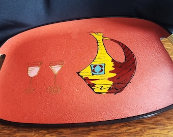 May include: A red oval serving tray with black trim and white handles. The tray features a hand-painted design of a yellow and red decanter with a blue and yellow square on the front, and two pink glasses with gold stems.