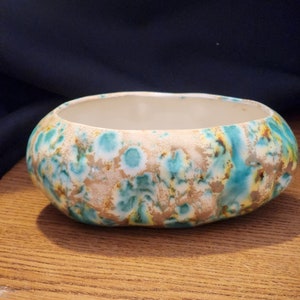 May include: A white ceramic bowl with a mottled glaze in shades of teal, brown, and white. The bowl has a rounded shape and a slightly rippled rim.