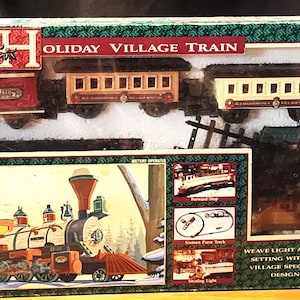 Könnte beinhalten: Ein Holiday Village Train Spielzeugeisenbahn-Set in einer rechteckigen Schachtel. Das Set enthält eine rote Lokomotive, einen roten Kohlewagen, einen beigen Personenwagen, einen weißen Personenwagen und einen roten Begleitwagen. Die Schachtel zeigt Illustrationen.
