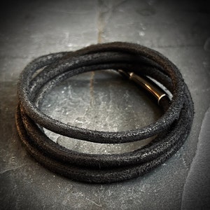 Pulsera de cuero negro envejecido minimalista hecha a mano por artesanos, con cierre de seguridad mate cepillado.