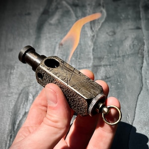 May include: A brass keychain lighter with a textured surface and a small ring. The lighter is being held in a hand.