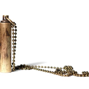 May include: A brass pendant with a chain. The pendant is cylindrical and has a textured surface.