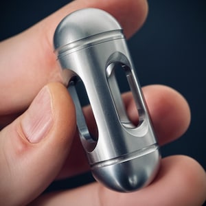 Op de afbeelding: Een zilveren metalen fidget-speelgoed met een cilindrische vorm en een hol centrum. Het speelgoed heeft een gladde, gepolijste afwerking en is ontworpen om in de hand te worden gedraaid en gemanipuleerd.