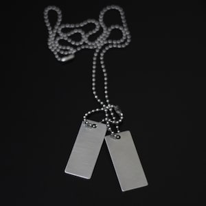 May include: Two silver dog tags on a silver chain. The tags are blank and rectangular.