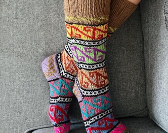 May include: Knee-high socks with a brown cuff and a colorful geometric pattern. The socks feature a mix of colors including pink, purple, green, orange, and black. The socks are made of a thick, knitted material.