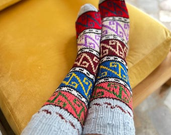 May include: A pair of colorful, patterned socks with a gray cuff and a variety of geometric designs in red, blue, pink, and purple. The socks are resting on a yellow chair.