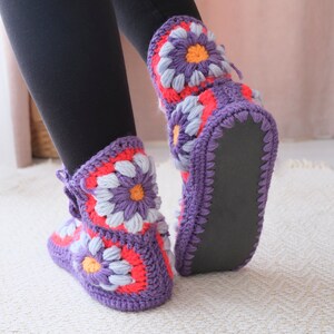 May include: Purple crochet slippers with a floral design featuring pink, white, and orange accents. The slippers have a black rubber sole.