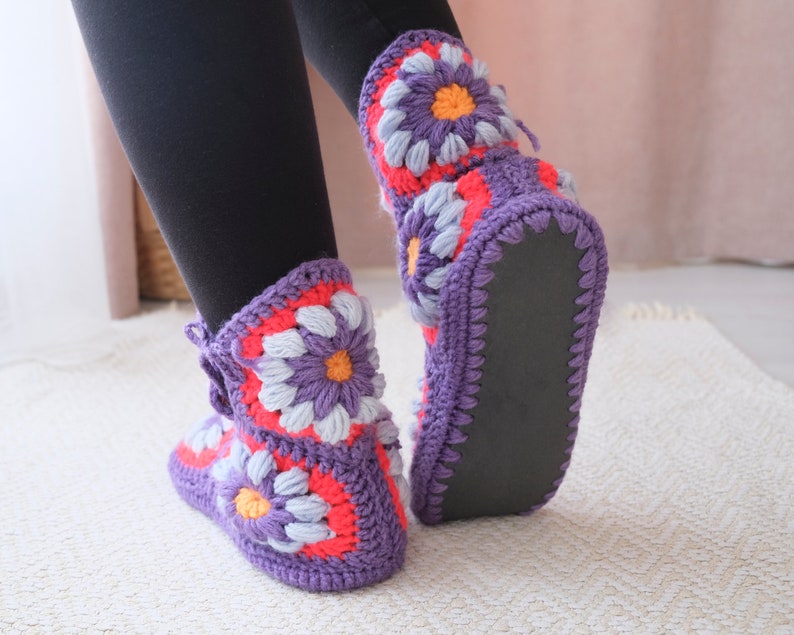 May include: Purple crochet slippers with a floral design featuring pink, white, and orange accents. The slippers have a black rubber sole.