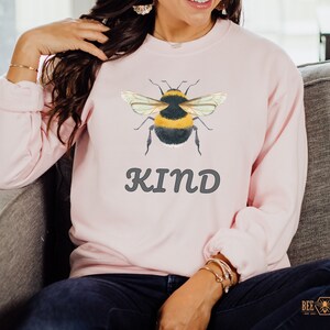 May include: A pink sweatshirt with a bumble bee graphic and the word "KIND" in gray lettering.