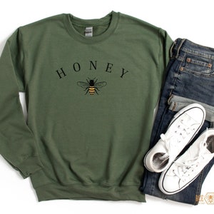 May include: A green sweatshirt with the word "HONEY" printed in black letters above a black and yellow bee illustration.