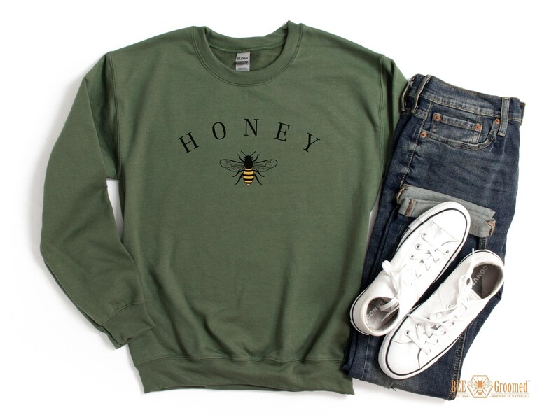 May include: A green sweatshirt with the word "HONEY" printed in black letters above a black and yellow bee illustration.