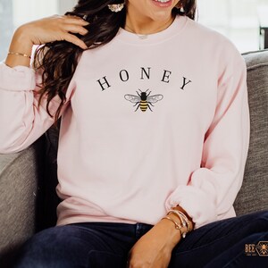 May include: A pink sweatshirt with the word "HONEY" printed in black above a small black and yellow bee graphic.