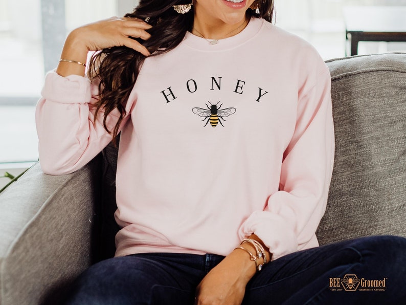 May include: A pink sweatshirt with the word "HONEY" printed in black above a small black and yellow bee graphic.