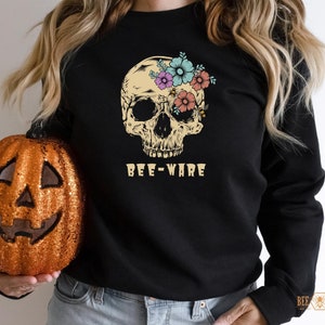 May include: Black long-sleeved shirt with a floral skull graphic and the text "Bee-Ware".