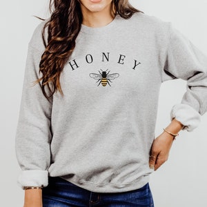 May include: A gray sweatshirt with the word "HONEY" printed in black letters above a small black and yellow bee graphic.