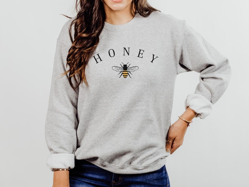 May include: A gray sweatshirt with the word "HONEY" printed in black letters above a small black and yellow bee graphic.