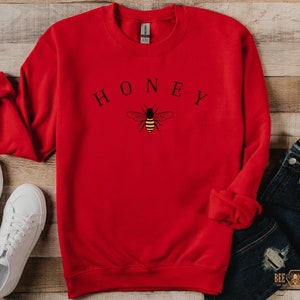 May include: Red sweatshirt with a bee and the word "HONEY" printed on the front.