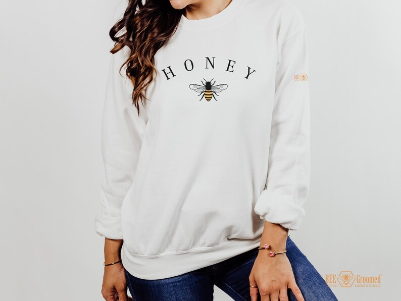 May include: White sweatshirt with the word "HONEY" printed in black letters and a small bee graphic in black and yellow.