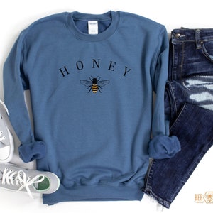 May include: A blue sweatshirt with the word "HONEY" printed in black letters and a small bee graphic in yellow and black.