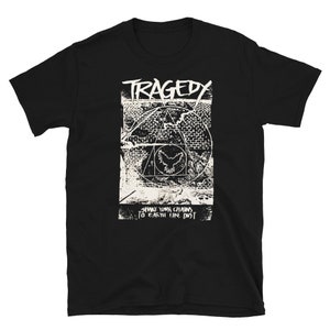 May include: Black t-shirt with a distressed white graphic. The graphic includes the word "TRAGEDY" above a geometric design with a bird-like emblem and the text "SHAKE YOUR CHAINS TO EARTH LIKE DUST".