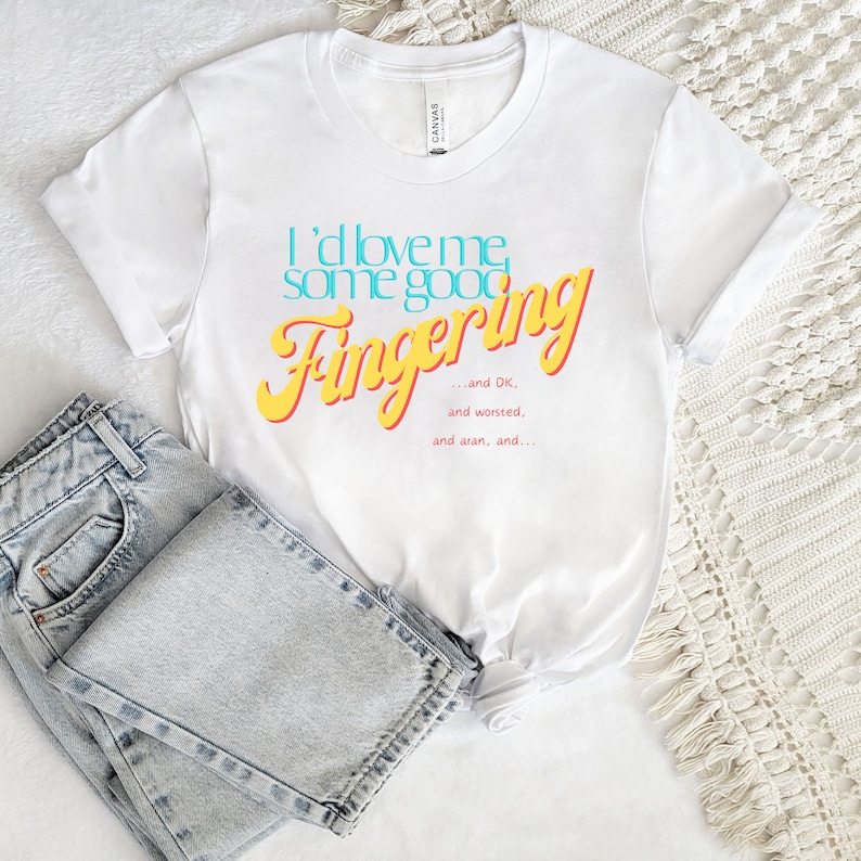 May include: White t-shirt with the text "I'd love me some good Fingering... and DK, and worsted, and aran, and..." in yellow and blue lettering.