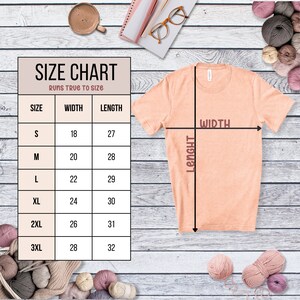 May include: Size chart for a t-shirt with measurements in inches for width and length. The chart shows sizes S through 3XL. The t-shirt is peach colored and is shown on a wooden background.