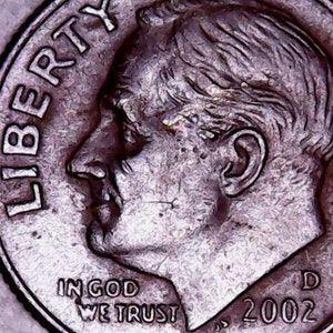 May include: Close-up of a silver US dime coin with the inscription "LIBERTY" on the left side and "IN GOD WE TRUST" and "2002" on the bottom. The coin features a profile of a man's face.