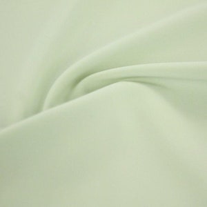 Pode incluir: Um tecido macio de cor verde claro com uma textura suave e fluida. O tecido está dobrado em uma curva suave, destacando seu caimento e seu brilho sutil.