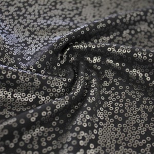May include: Black fabric with a silver sequin pattern. The fabric is wrinkled and has a soft, flowing texture.