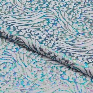 May include: White fabric with a pattern of iridescent teal and silver animal prints, including leopard spots and zebra stripes. The fabric is folded, showing the texture and design. The overall theme is a modern, abstract animal print.