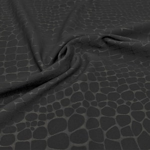 Op de afbeelding: Zwarte stof met een subtiel, getextureerd patroon dat lijkt op reptielschubben. De stof is gedrapeerd, waardoor plooien en schaduwen ontstaan die de diepte en dimensie van het patroon benadrukken. Een donker, elegant textiel.