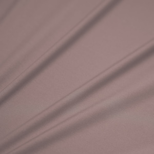Op de afbeelding: Een gladde, zachte en licht gestructureerde stof in een gedempte mauve kleur. De stof is gedrapeerd en gevouwen, waardoor zachte plooien en bochten ontstaan.
