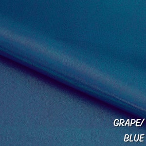 May include: Close-up of a textured fabric in a deep blue color. The fabric has a subtle shimmer and is labeled "GRAPE/BLUE".