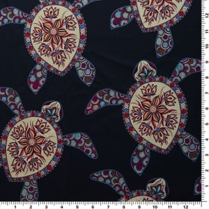 Op de afbeelding: Een donkerblauwe stof met een herhalend patroon van gestileerde zeeschildpadden. Elke schildpad heeft een cirkelvormig ontwerp met ingewikkelde details in beige, bruin, rood en paarse tinten.