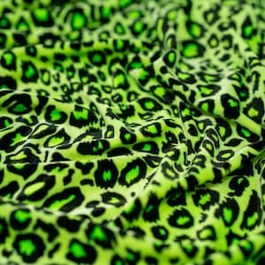 Könnte beinhalten: Nahaufnahme eines grünen und schwarzen Stoffes mit Leopardenmuster. Der Stoff ist weich und hat eine samtige Textur.