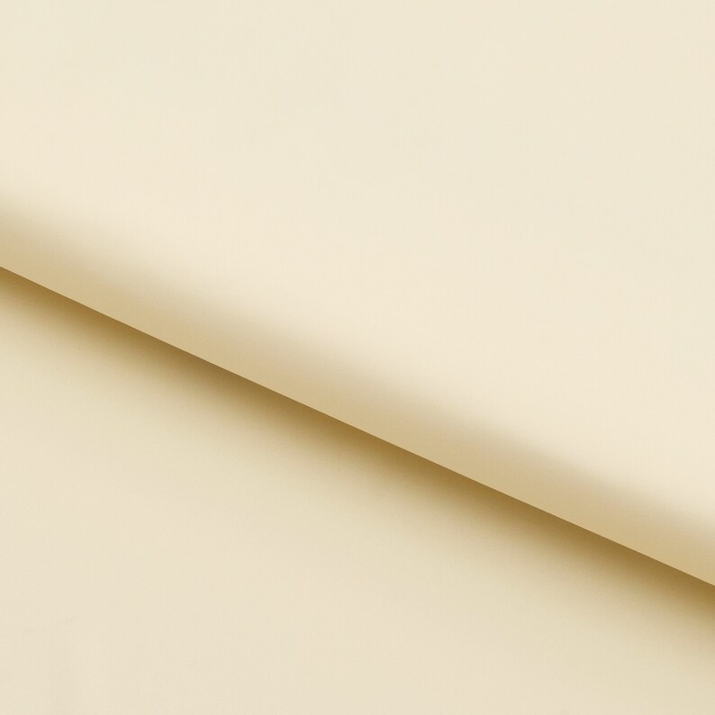 Pu&ograve; includere: Primo piano di una superficie liscia di colore avorio con una piega diagonale sottile. La superficie &egrave; illuminata uniformemente e sembra essere fatta di un materiale morbido e flessibile.