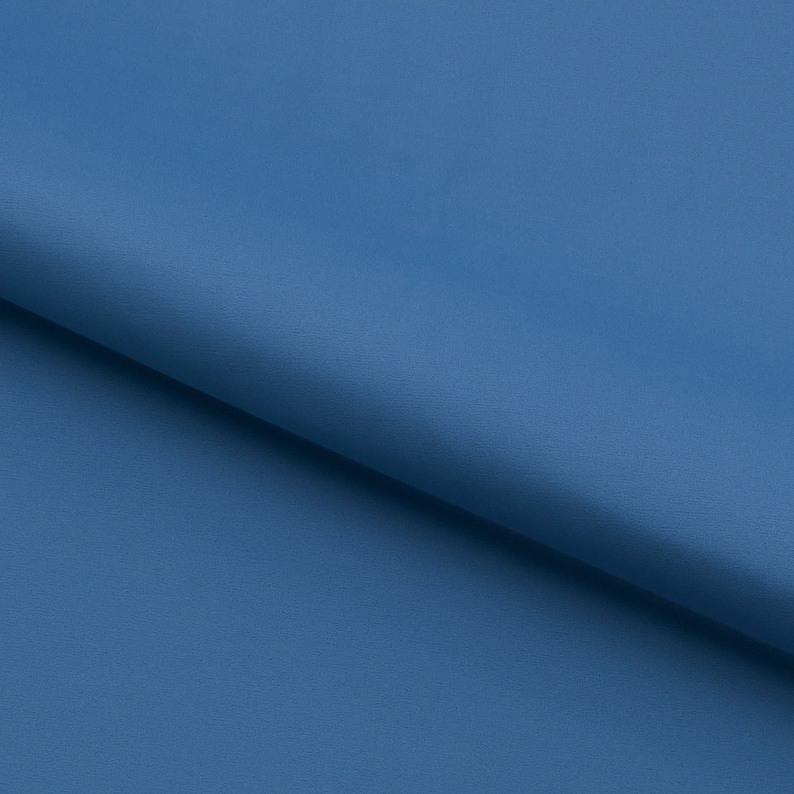 Pu&ograve; includere: Un primo piano di un tessuto liscio di colore blu solido. Il tessuto &egrave; piegato a met&agrave;, creando una linea diagonale attraverso l'immagine.