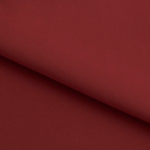 May include: A close-up of a smooth, deep red fabric. The fabric has a subtle texture and a rich, burgundy hue.