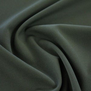 May include: Close-up of a dark green fabric with a smooth, slightly textured surface. The fabric is folded and draped, showing its soft and flowing nature.