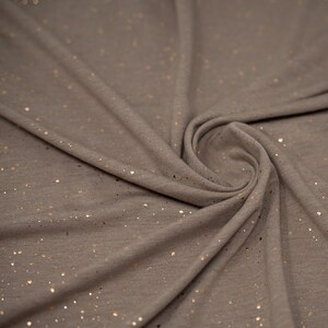 May include: A close-up of a gray fabric with a subtle shimmer of gold glitter. The fabric is soft and has a slightly textured surface.